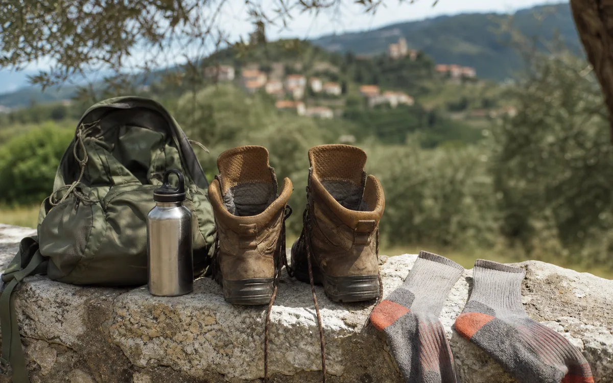 Scarponi aperti e calze tecniche ad asciugare su un muretto durante una pausa